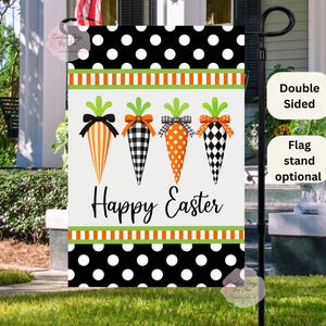 May include: A double-sided Easter garden flag featuring four carrot designs with green tops and patterned bows. The carrots are orange, black and white, and the flag has a black and white polka dot border with the words "Happy Easter".