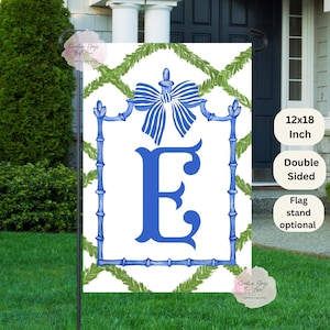 May include: A white garden flag with a blue monogram "E" in a blue and white frame with a blue bow on top. The flag is surrounded by green leafy vines. The flag is 12x18 inches and double-sided. A flag stand is optional.