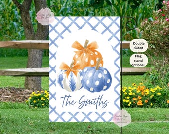 May include: A double-sided garden flag featuring three watercolor pumpkins in orange and blue with white polka dots and bows. The flag has a blue and white plaid border and the family name "The Smiths" in script.