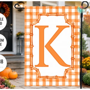 May include: A rectangular garden flag featuring an orange and white buffalo check pattern. In the center, a white rectangular field is enclosed by an orange bamboo-style frame, containing a large, bold, orange capital letter K.
