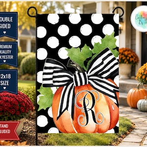 May include: A rectangular garden flag featuring a black background with white polka dots. An orange pumpkin with green leaves is centered, adorned with a large black and white striped bow and a black letter R monogram in a decorative script font.