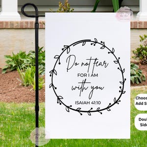 May include: A white garden flag with the text "Do not fear, for I am with you, Isaiah 41:10" in a black floral wreath. The flag is double-sided and can be purchased with a stand.