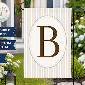 May include: A rectangular garden flag featuring a cream and beige vertical striped pattern. In the center, a large dark brown capital letter B is enclosed within a thin oval frame. The flag measures 12x18 inches and is double-sided.