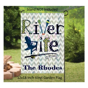 May include: A 12x18 inch vinyl garden flag with a gray chevron pattern. The flag features the text "River Life" in blue and yellow letters with a fishing rod and a blue and white Adirondack chair. The text "The Rhodes" is printed in blue at the bottom of the flag.