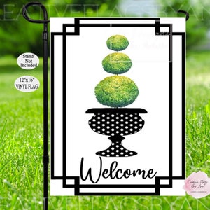 May include: A black and white welcome garden flag with a black and white polka dot planter and a green topiary bush. The flag reads "Welcome".