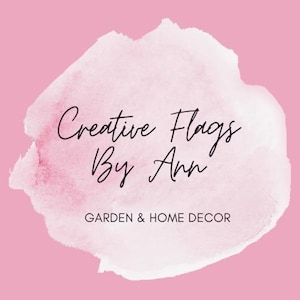 May include: A logo for "Creative Flags By Ann" on a pink background. The text is in black script, with a watercolor-style white and pink shape behind it. Below the name, the text reads "GARDEN & HOME DECOR".