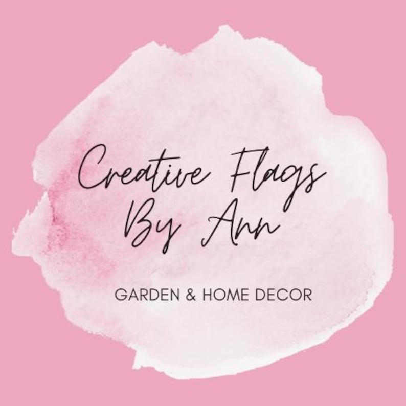 May include: A logo for "Creative Flags By Ann" on a pink background. The text is in black script, with a watercolor-style white and pink shape behind it. Below the name, the text reads "GARDEN & HOME DECOR".