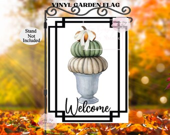 May include: A white vinyl garden flag with a black border and the word "Welcome" in black lettering. The flag features a watercolor illustration of a stack of three pumpkins in a gray planter.