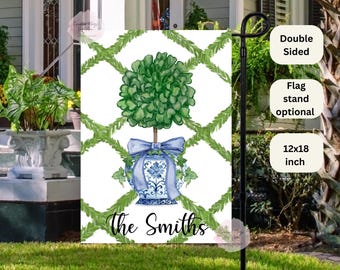 May include: A 12x18 inch double-sided garden flag with a white background and a green topiary in a blue and white planter. The flag has a green and white trellis pattern and the text "The Smiths" at the bottom.