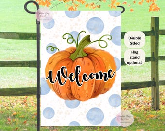 May include: A double-sided garden flag featuring a watercolor-style orange pumpkin with the word "Welcome" in black script. The background has blue polka dots. A flag stand is optional.