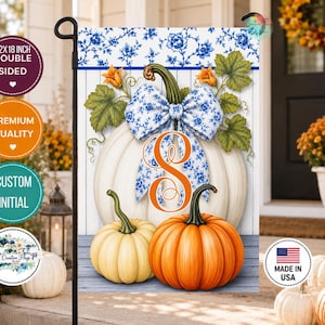 May include: A decorative garden flag featuring a large white pumpkin with a blue and white floral bow and the orange letter S. Below, a smaller cream pumpkin and a bright orange pumpkin sit on a blue wooden surface. The flag measures 12x18 inches.