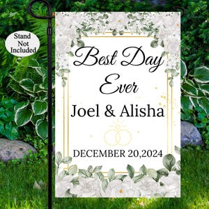May include: White garden flag with gold trim and floral design. The text reads "Best Day Ever" with the names "Joel & Alisha" and the date "December 20, 2024".