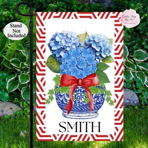 May include: A white garden flag with a red and white geometric pattern border. A blue and white porcelain vase with a red bow holds a bouquet of blue hydrangeas. The text "SMITH" is printed in black at the bottom of the flag.