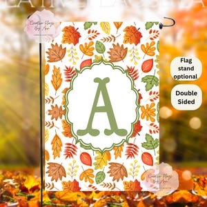 May include: A double-sided garden flag featuring a fall leaves pattern in shades of orange, yellow, and green. A large green letter "A" is centered within a decorative frame. The flag is designed for outdoor use.
