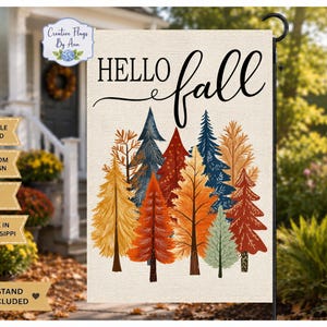 May include: A rectangular garden flag with a cream-colored background featuring the text "HELLO fall" in black script and block lettering. Below the text is a colorful illustration of stylized pine trees in shades of orange, red, blue, and yellow.