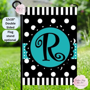May include: A double-sided garden flag, 12x18 inches, with a black and white polka dot and stripe design. The flag features a teal circle with a large black letter "R". The flag is displayed on a black metal stand in a grassy yard.