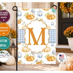 May include: A rectangular garden flag featuring a repeating pattern of orange and light blue pumpkins with small birds on a white background. A central scalloped white frame contains a large orange letter M over a light blue gingham stripe.