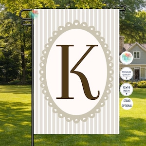 May include: A rectangular garden flag featuring a vertical beige and white striped background. In the center, a large dark brown letter K is displayed inside a white oval frame with a scalloped edge. The flag includes text stating 12x18 inch.