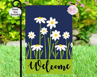 May include: A welcome garden flag with a navy blue background and white daisies with yellow centers. The bottom of the flag has a green banner with the word "Welcome" in black cursive writing.