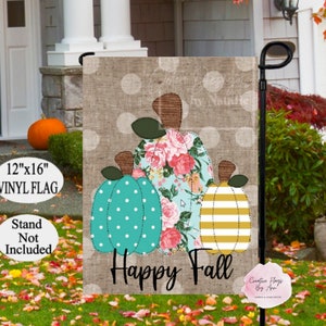 May include: A 12" x 16" vinyl flag featuring three decorative pumpkins with floral, polka dot, and striped patterns. The flag has the words "Happy Fall" and is displayed outdoors. The stand is not included.
