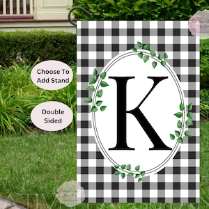 May include: A double-sided garden flag with a black and white checkered pattern. The flag features a white oval with the letter "K" in black, surrounded by a green leaf design. The text "Choose To Add Stand" and "Double Sided" are also visible.