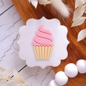 May include: A white cookie cutter shaped like a cupcake with pink frosting and yellow sprinkles.