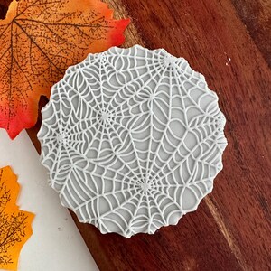 Può includere: Biscotto rotondo bianco decorato con un design dettagliato di ragnatela bianca.