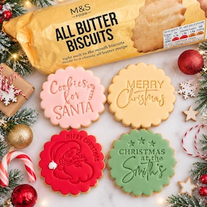 May include: Four round scalloped biscuits with embossed designs: a pink biscuit reading Cookies for SANTA, a yellow one saying MERRY Christmas, a red one with a Santa face, and a green one reading CHRISTMAS at the Smith's, near an M&S biscuit packet.