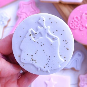 Op de afbeelding: Een lichtblauwe suikerkoek versierd met een wit silhouet van een vrouw in een jurk en gouden glitter.