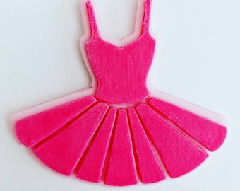 Op de afbeelding: Een roze ballerina tutu met een lichtroze omtrek. De tutu heeft een lijfje met spaghettibandjes en een uitlopende rok. Het ontwerp is effen van kleur en lijkt een koekjessteker of een soortgelijk knutselartikel te zijn.