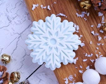 Op de afbeelding: Een witte sneeuwvlokvormige koek op een houten oppervlak met witte sprinkles. De koek is versierd met een lichtblauwe glazuur.