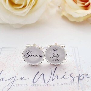 May include: A pair of silver cufflinks with white enamel. One cufflink says "Groom" and the other says "24th July 2021".