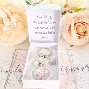 May include: A white gift box with a silver charm keychain inside. The keychain has a pink circle with the text "An amazing coworker is hard to find, different to part with and impossible to forget." The box has a card inside that says "Dear Wendy. We will truly miss you and we wish you all the best in future."