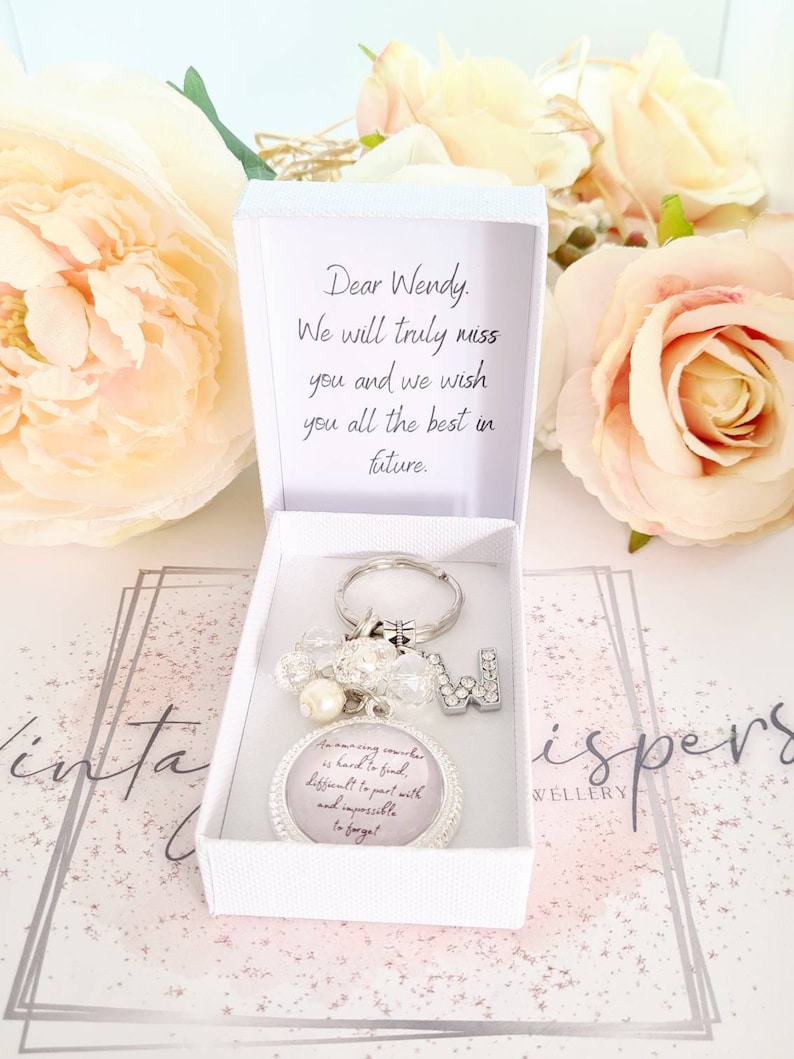 May include: A white gift box with a silver charm keychain inside. The keychain has a pink circle with the text "An amazing coworker is hard to find, different to part with and impossible to forget." The box has a card inside that says "Dear Wendy. We will truly miss you and we wish you all the best in future."