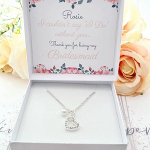 May include: A white box with a floral design and the text "Rosie I couldn't say "I Do" without you... Thank you for being my Bridesmaid" inside. The box contains a silver necklace with a heart pendant and a pearl.