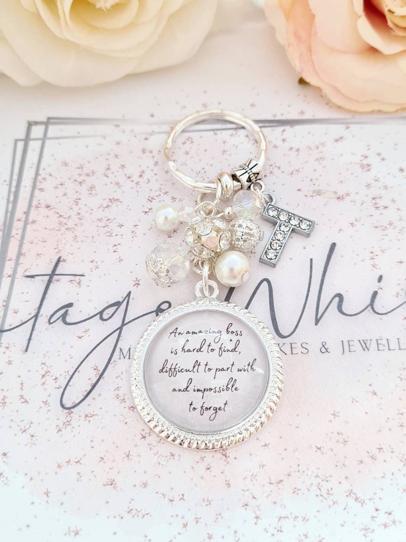 May include: A silver keychain with a charm that says "An amazing boss is hard to find, difficult to part with and impossible to forget". The charm is surrounded by small white beads and a silver letter T.