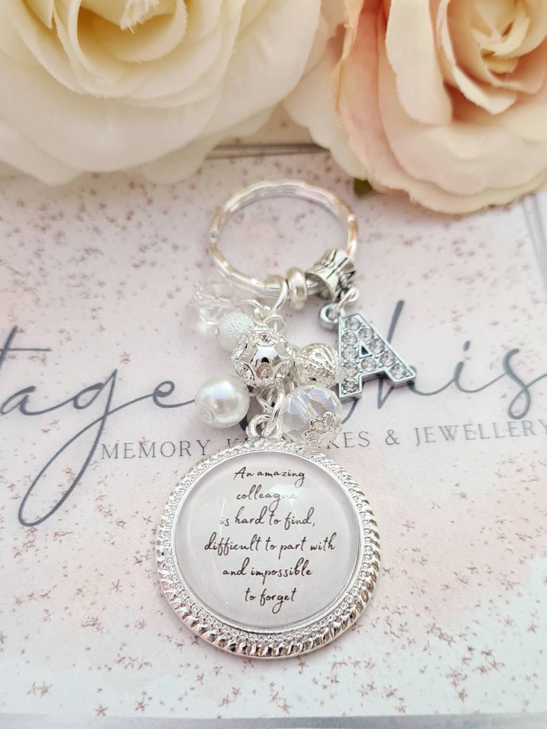 May include: Silver keychain with a charm that reads "An amazing colleague is hard to find, difficult to part with and impossible to forget". The keychain also has a silver letter A charm and other decorative charms.