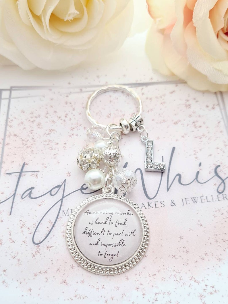 May include: A silver keychain with a charm that reads "An amazing coworker is hard to find, difficult to part with and impossible to forget". The charm is surrounded by white and clear beads.