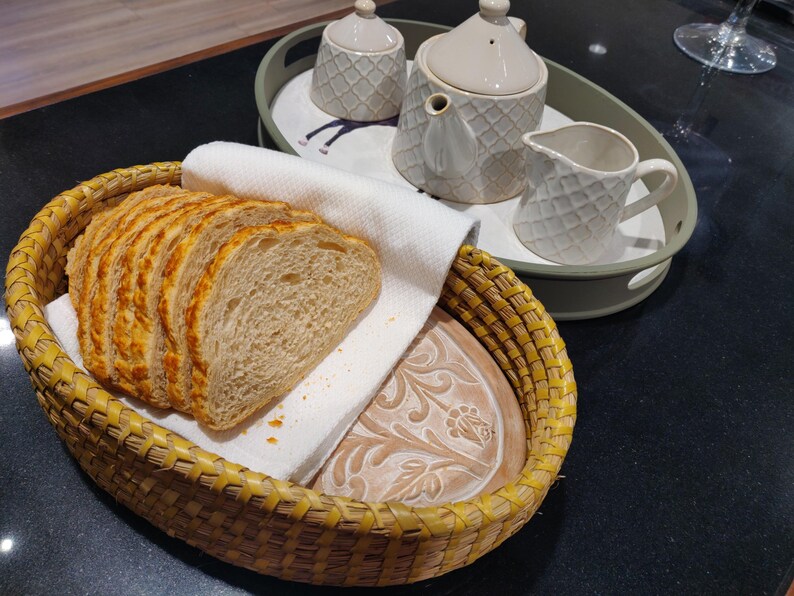 Puede incluir: Una cesta ovalada de mimbre amarillo que contiene varias rebanadas de pan sobre un pa&ntilde;o blanco, junto a una bandeja verde claro con una tetera, un azucarero y una jarra de crema color crema, con un patr&oacute;n de diamantes texturizado.