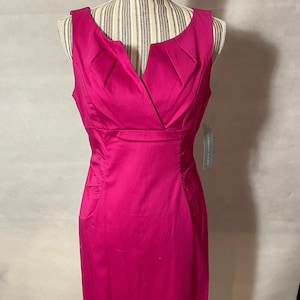 Könnte beinhalten: Ein ärmelloses fuchsia-rosa Kleid mit V-Ausschnitt und figurbetonter Silhouette. Das Kleid hat eine Faltendetail am Ausschnitt und ein kleines Etikett mit der Aufschrift "London Times".