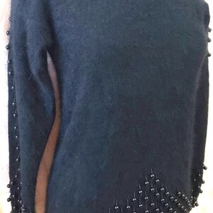 Könnte beinhalten: Schwarzer, flauschiger Pullover mit schwarzen Perlenbesatz am Ausschnitt und am unteren Saum.