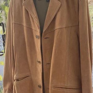 Puede incluir: Chaqueta de ante color canela con solapas, tres botones y dos bolsillos delanteros. La chaqueta está colgada de una percha de madera. La etiqueta dice "Marc New York".