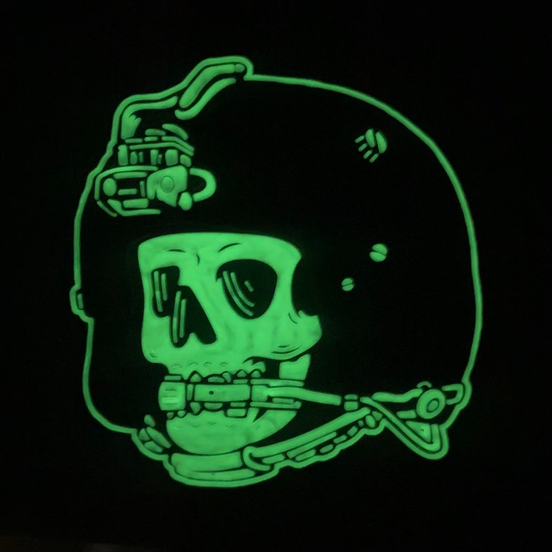 May include: A glow-in-the-dark skull wearing a helmet with a visor. The skull is wearing a mouth guard. The helmet has a design on the top.