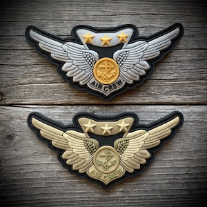 May include: Two embroidered patches with black backing, gold stitching, and a gold anchor with wings. The top patch has silver wings and the bottom patch has tan wings. Both patches say "AIR CREW" in black lettering.