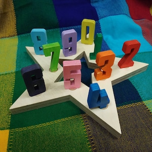 May include: A wooden star-shaped puzzle with colourful wooden numbers 0 through 9. The numbers are arranged in a circle around the star.