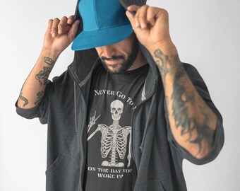 Peut inclure: Une personne portant un sweat à capuche gris foncé avec une fermeture éclair, une casquette de baseball bleue et un t-shirt noir avec un motif de squelette et le texte "Ne jamais aller dormir le jour où vous vous êtes réveillé".