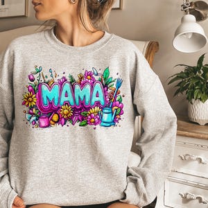May include: Gray sweatshirt with a colorful graphic design featuring the word "MAMA" surrounded by flowers, leaves, and gardening tools.