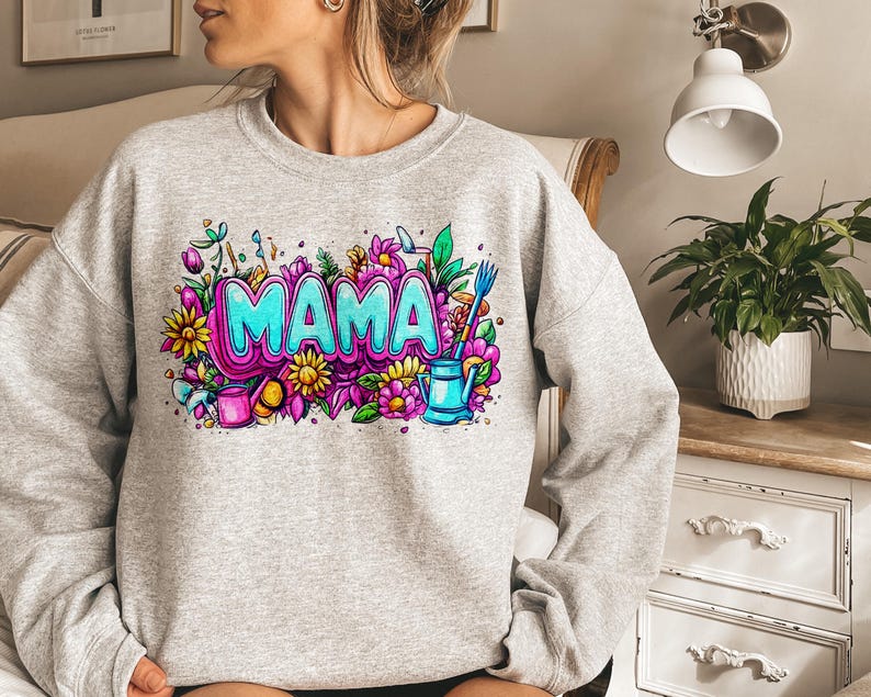 May include: Gray sweatshirt with a colorful graphic design featuring the word "MAMA" surrounded by flowers, leaves, and gardening tools.