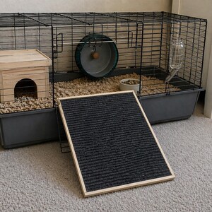 May include: A black wire cage for small pets, with a gray plastic base, a wooden house, a green exercise wheel, and a water bottle. A black ramp with a wooden frame is in front of the cage. The cage is on a light gray carpet.
