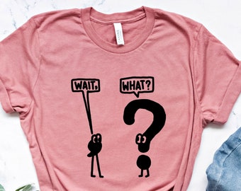 Op de afbeelding: Een roze T-shirt met een zwarte afbeelding van een stokfiguur dat een bord vasthoudt met de tekst "WAIT." en een ander stokfiguur dat een vraagteken vasthoudt met een bord met de tekst "WHAT?"